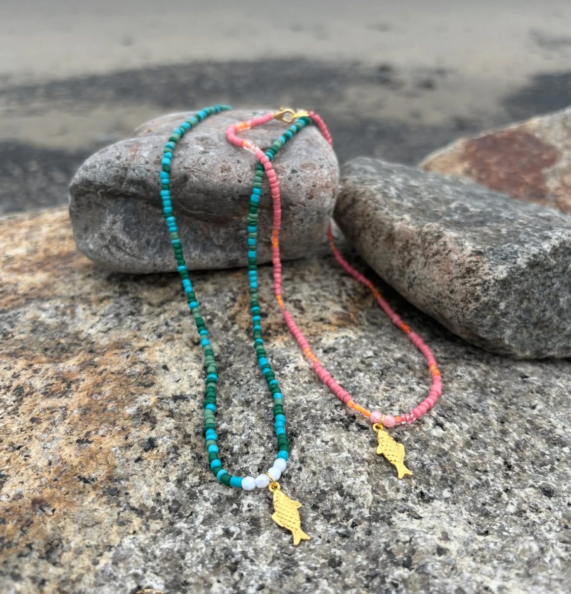 Two fish necklaces in teal and pink draped over Marblehead rocks