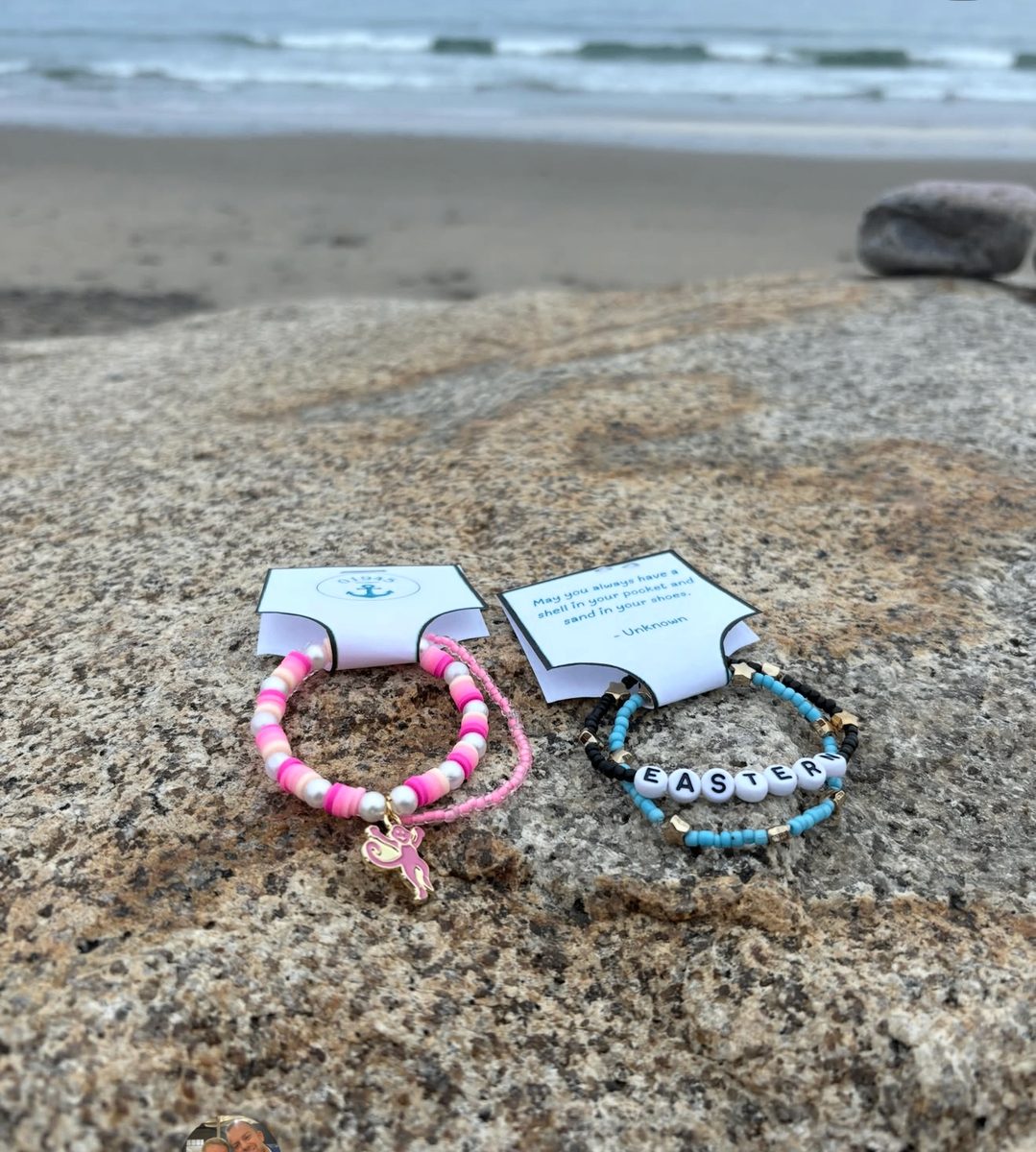 Two bracelets displayed on Marblehead rocks with branded cards and the ocean in the background
